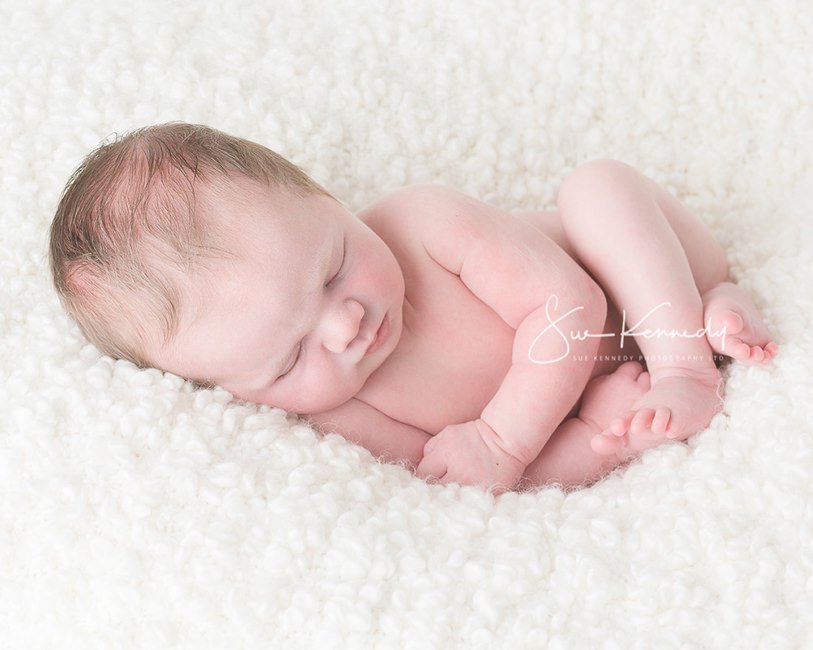 Sleeping newborn baby curl up on a soft blanket professionally photographed in Harlow, Essex