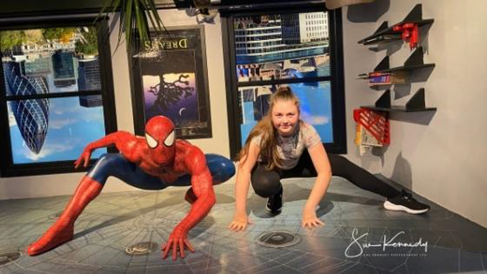 teenage girl matching the spiderman pose next to a life size model of the character