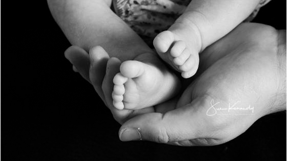 close up of tiny baby feet held in a fathers hands, black and white photograph