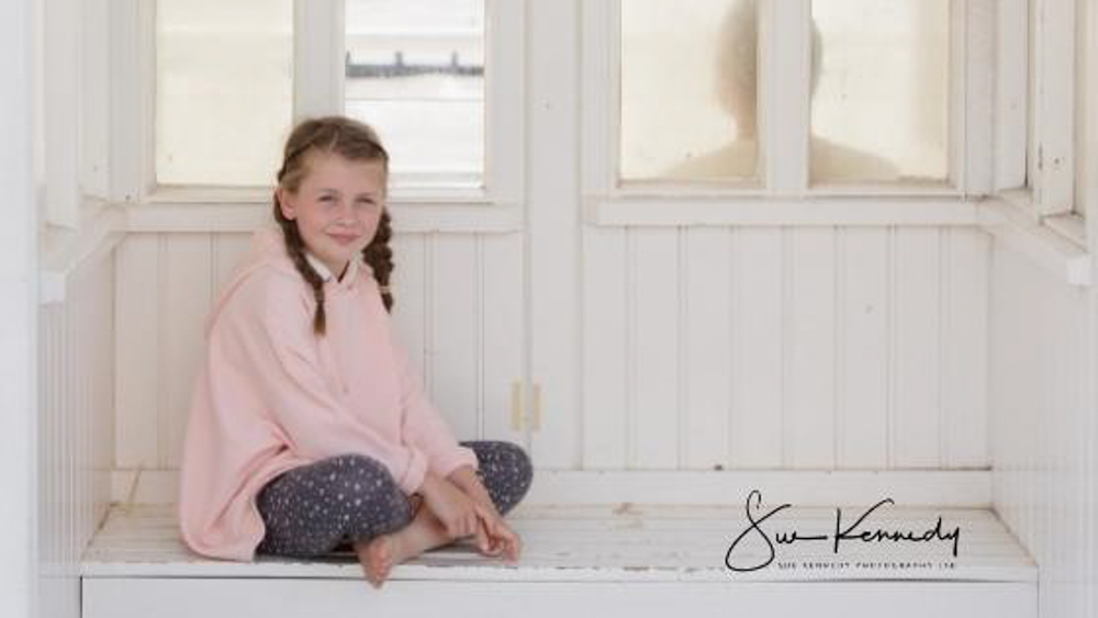 7 year old girl sitting crossed leg in a wooden seaside wind shelter