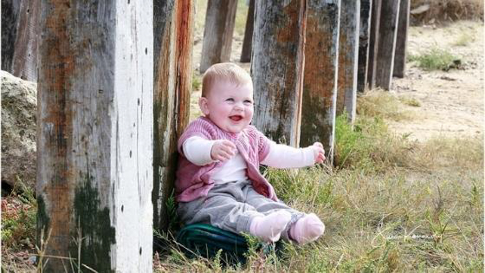 9 month old baby sitting on the ground, waving arms & smiling