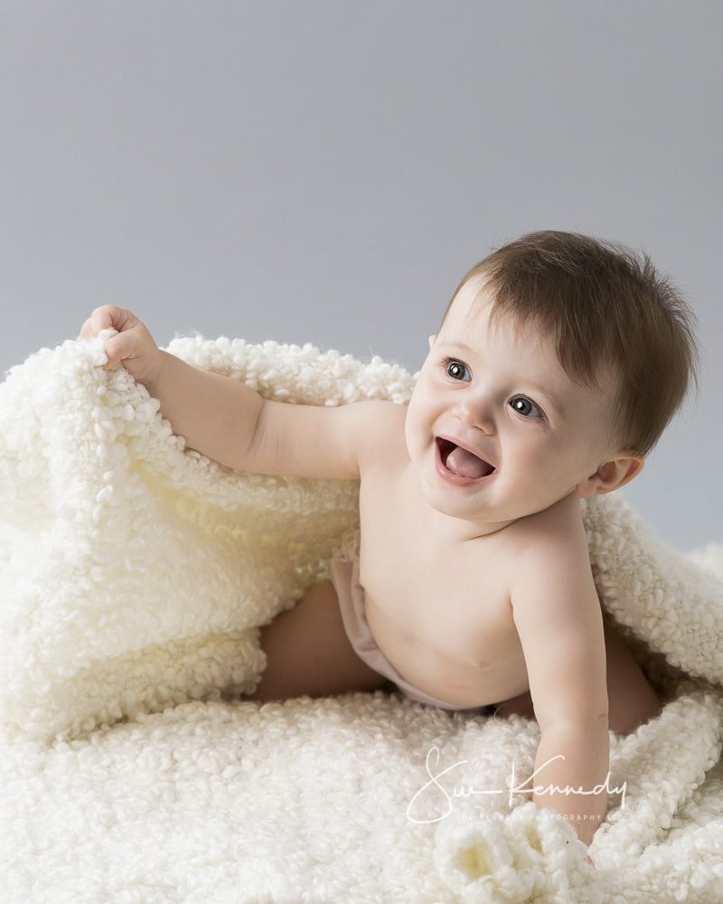 Baby girl pushing up from under a blanket during her portrait session at my photography studio in Harlow, Essex