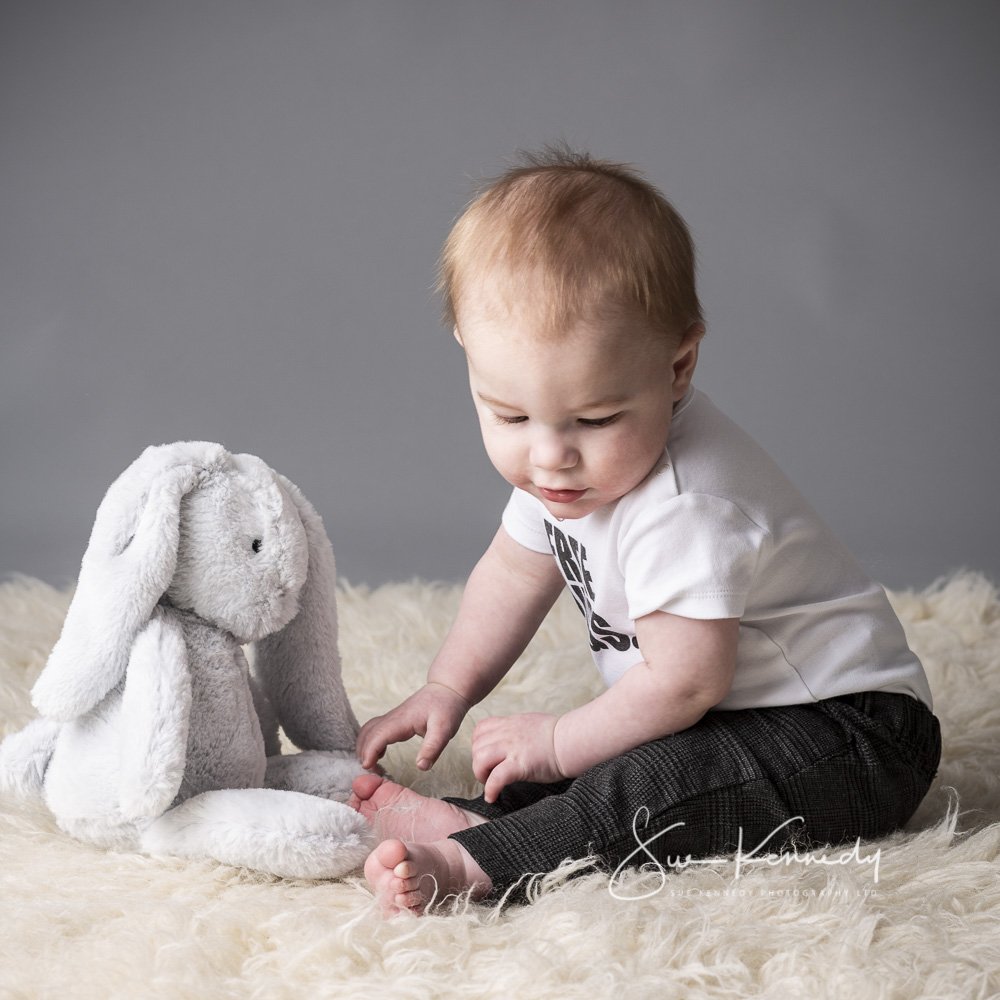 baby boy sat opposite his large soft toy - a bunny rabbit.