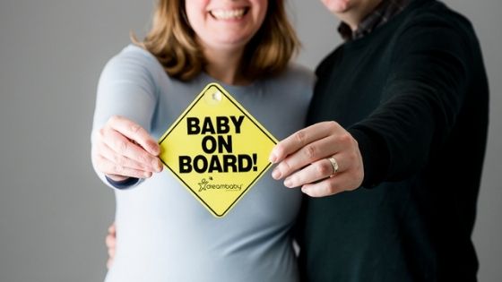Expecting parents holding a baby on board sign and smiling