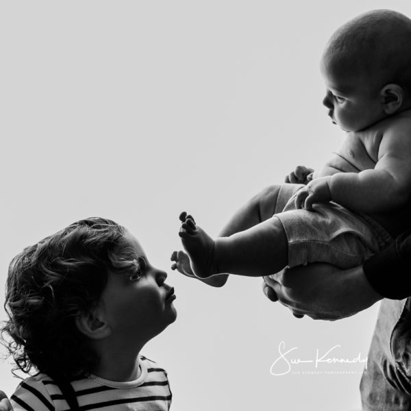 siblings interacting - kissing baby's toes - black and white photograph