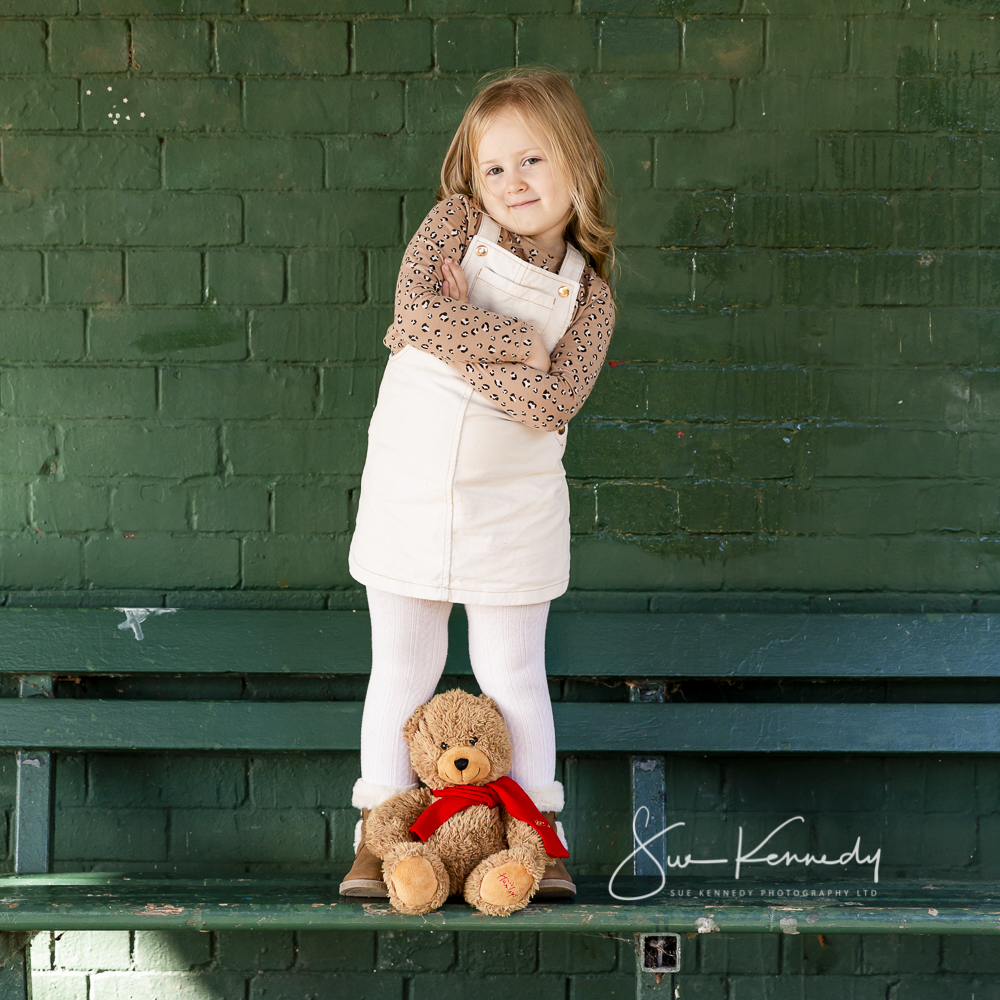 young girls stood on bench with her bear during child photoshoot