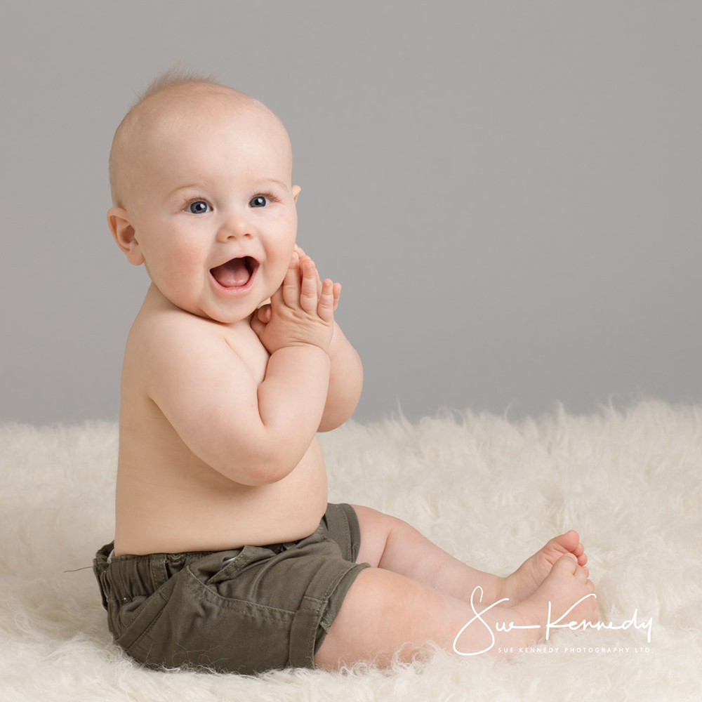 Baby boy sitting on a rug smiling towards camera during his baby photography session