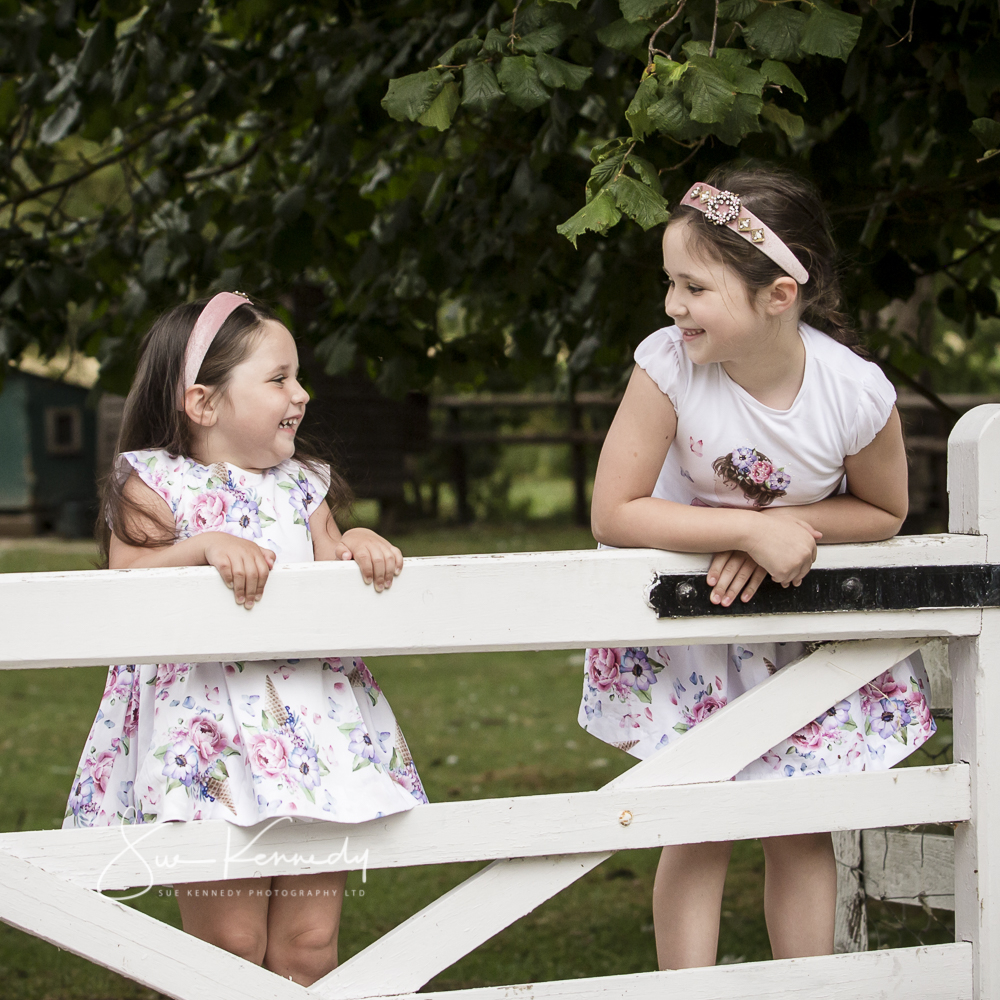 Two sisters climbing on a gate during an outdoor family portrait session at my studio's grounds in Harlow, Essex