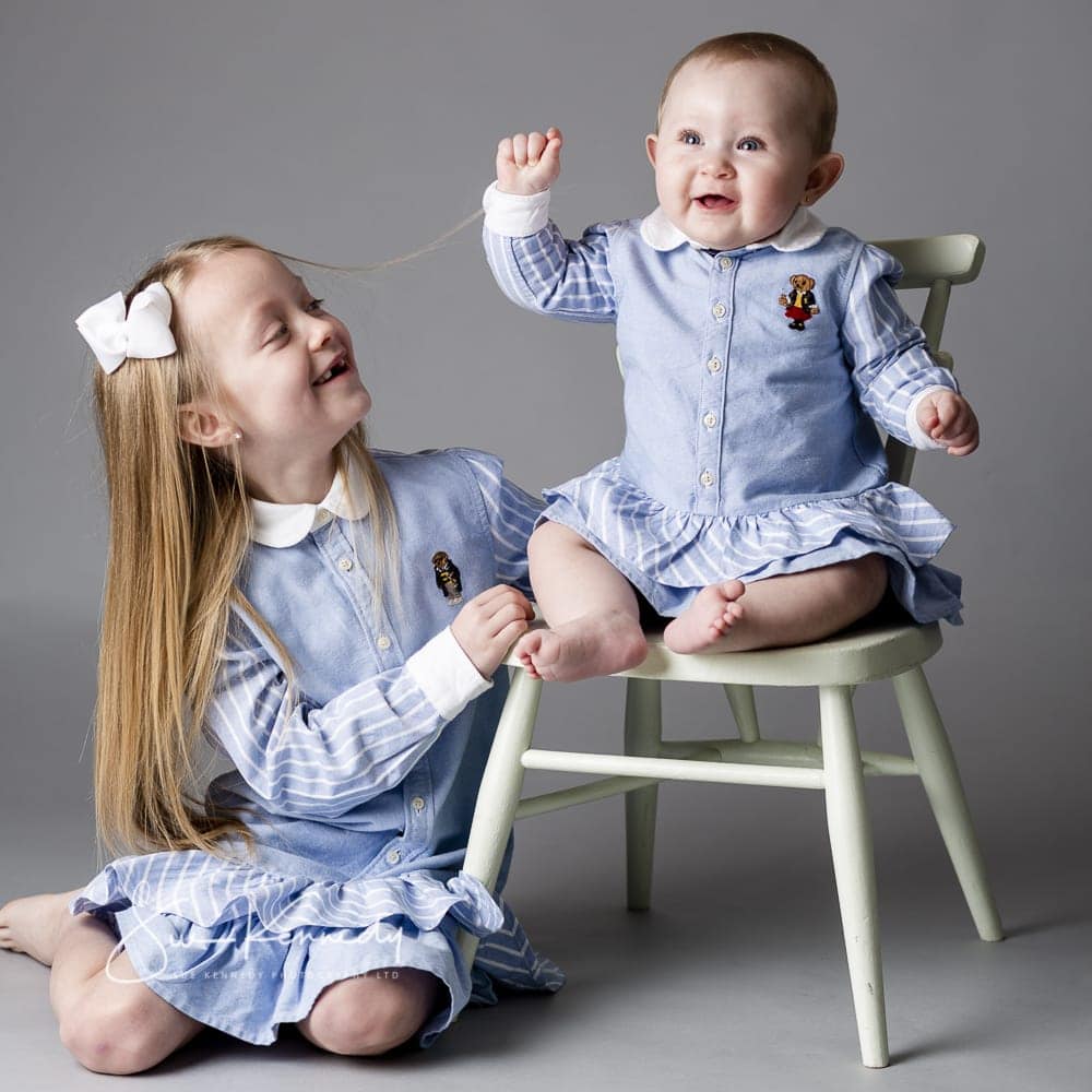 Big sister looking toward baby sister sitting laughing