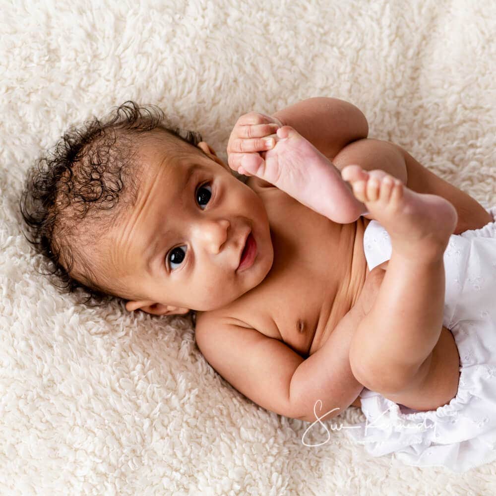 baby girl grabbing her feet during her photoshoot at my photography studio in Harlow. Essex