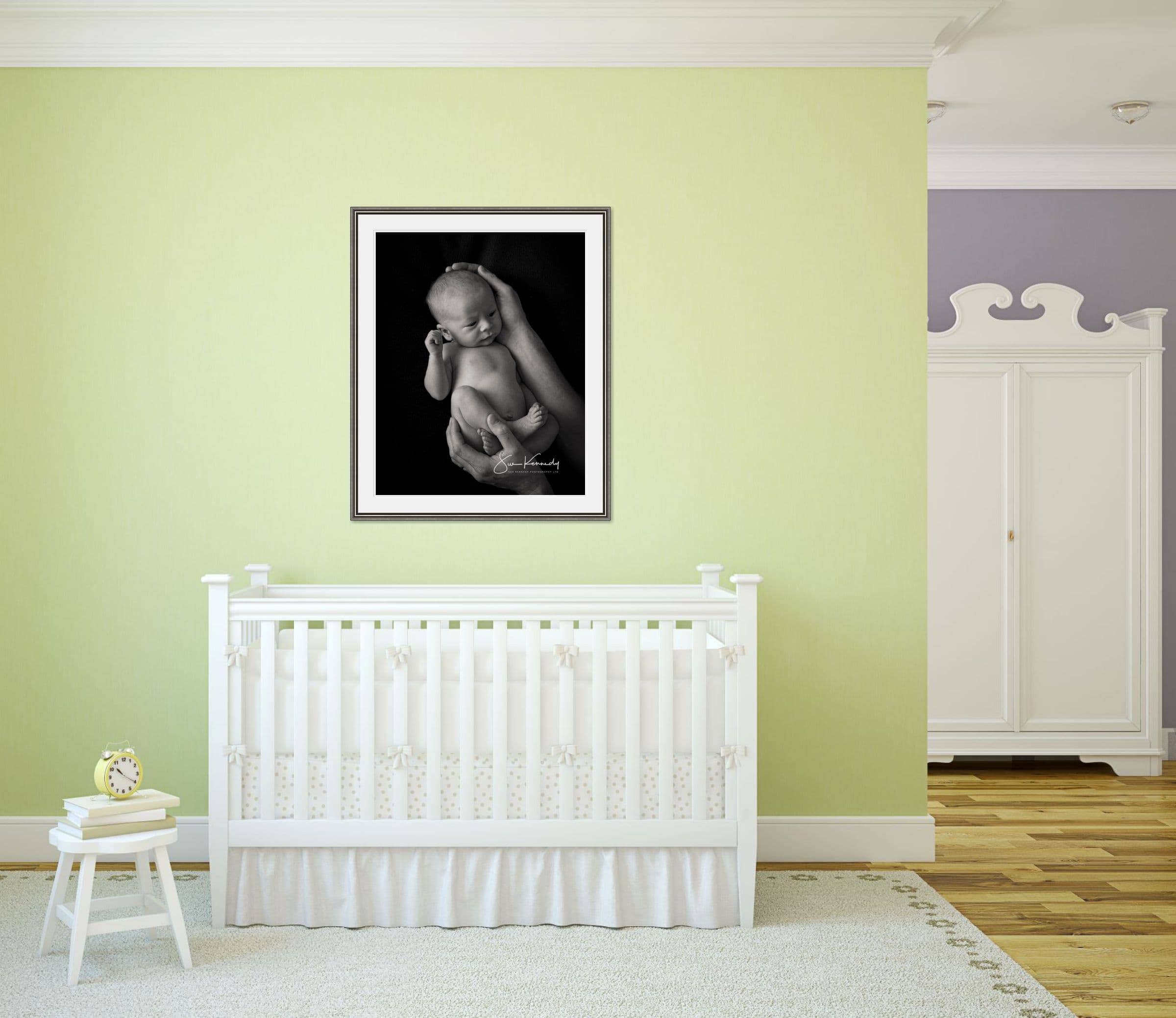 Room view of a nursery with a framed baby portrait on the wall above the baby's cot