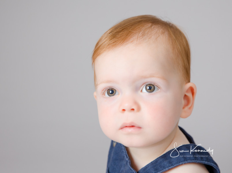 Close-up portrait of a baby with soft natural expression, photographed against a neutral background at Sue Kennedy Photography.