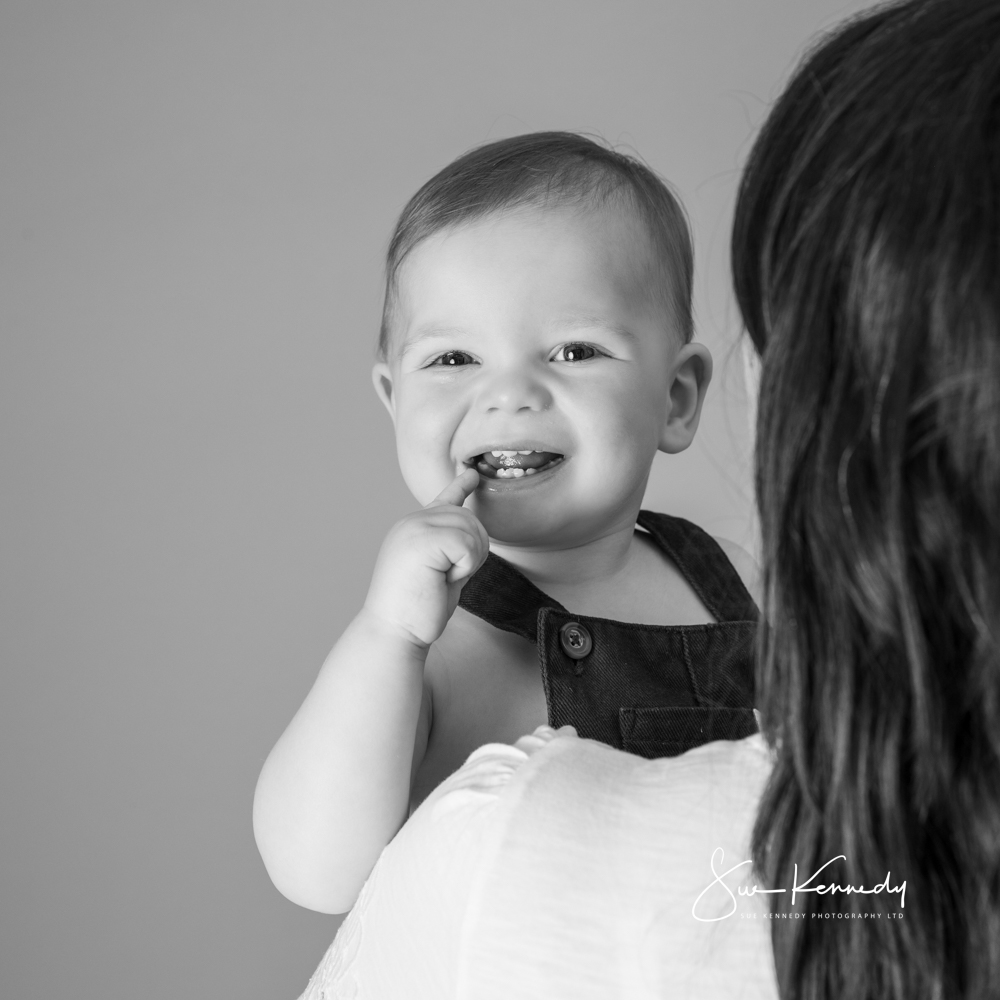 Baby smiling while being held by their mother during a relaxed, baby-led portrait at Sue Kennedy Photography.