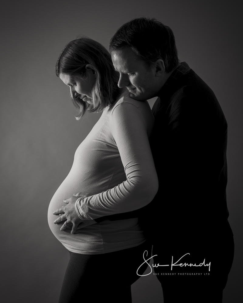 Parents to be looking down at baby bump. Black and white photo.
