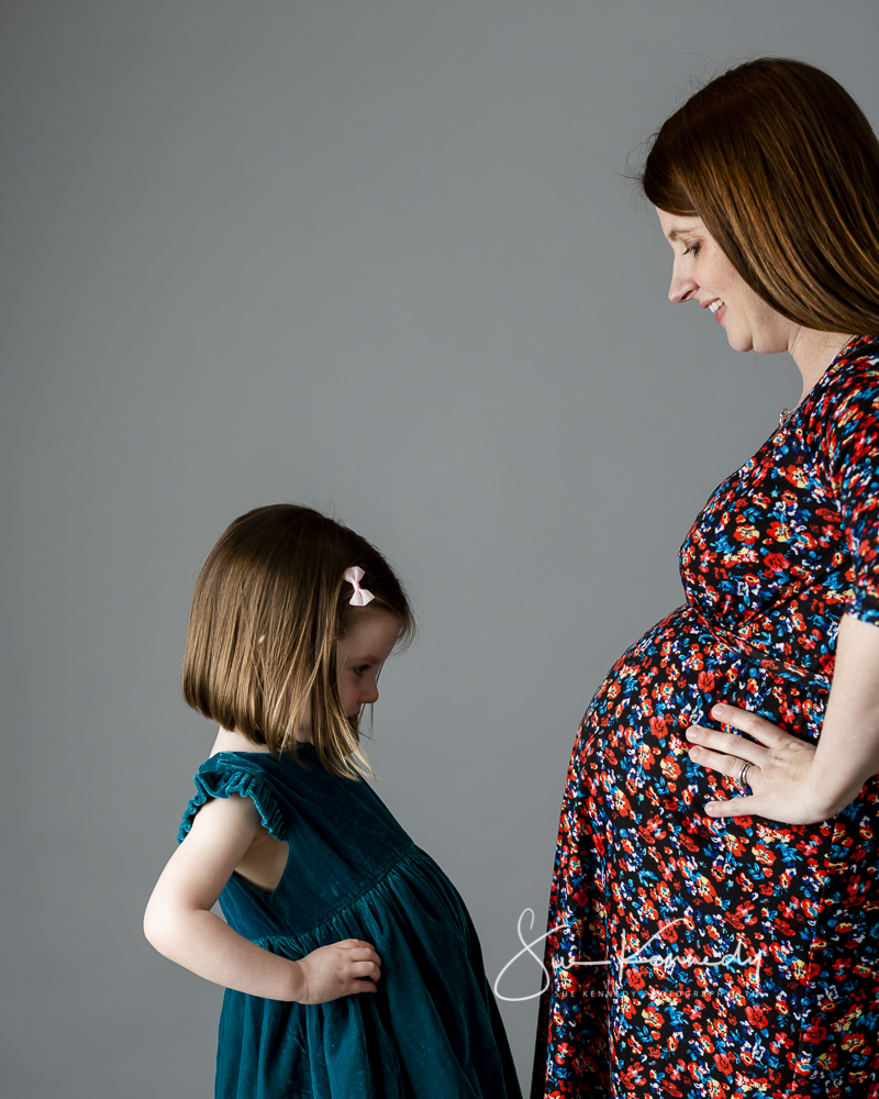 Pregnant mother and daughter in profile tummy to tummy