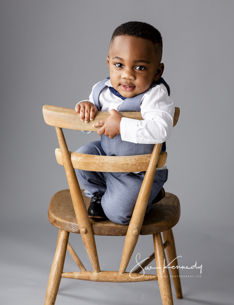 Toddler boy leaning over the back of a small chair smiling at camera