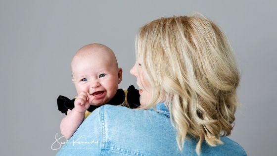 Young baby being cuddled my mum, but looking over her shoulder and smiling