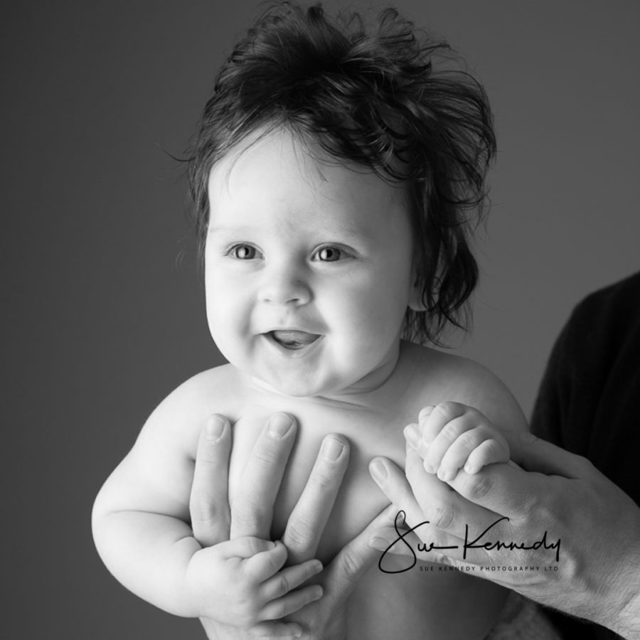 black & white of a baby boy smiling as he is held in his fathers arms