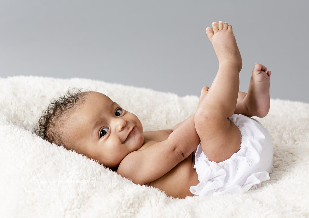 baby girl lying on her back kicking her legs in the air and looking toward the photographer