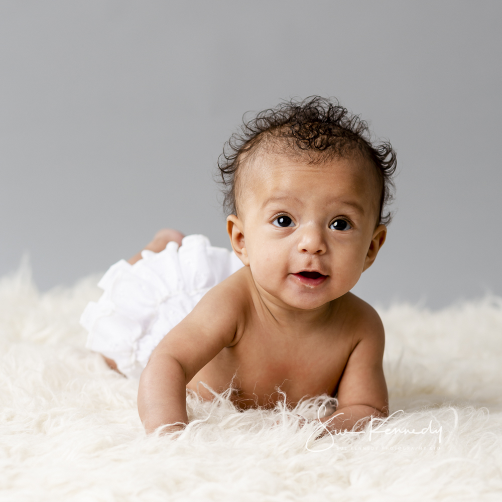 baby lying on her tummy on a rug looking toward camera with smiling eyes