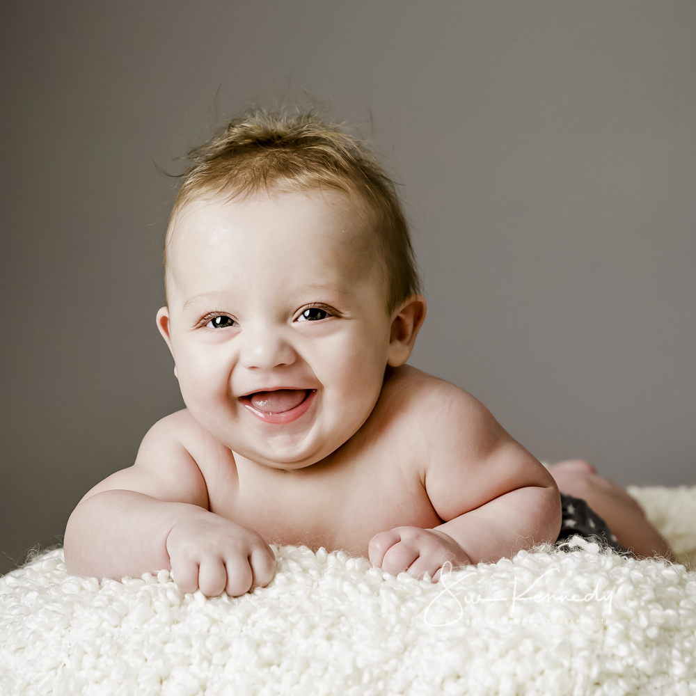 Baby laying on his tummy smiling to camera taken at a baby portrait session with Sue Kennedy photography