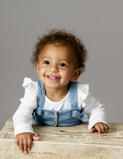baby smiling at the camera in an outfit of white t-shirt and denim dungarees