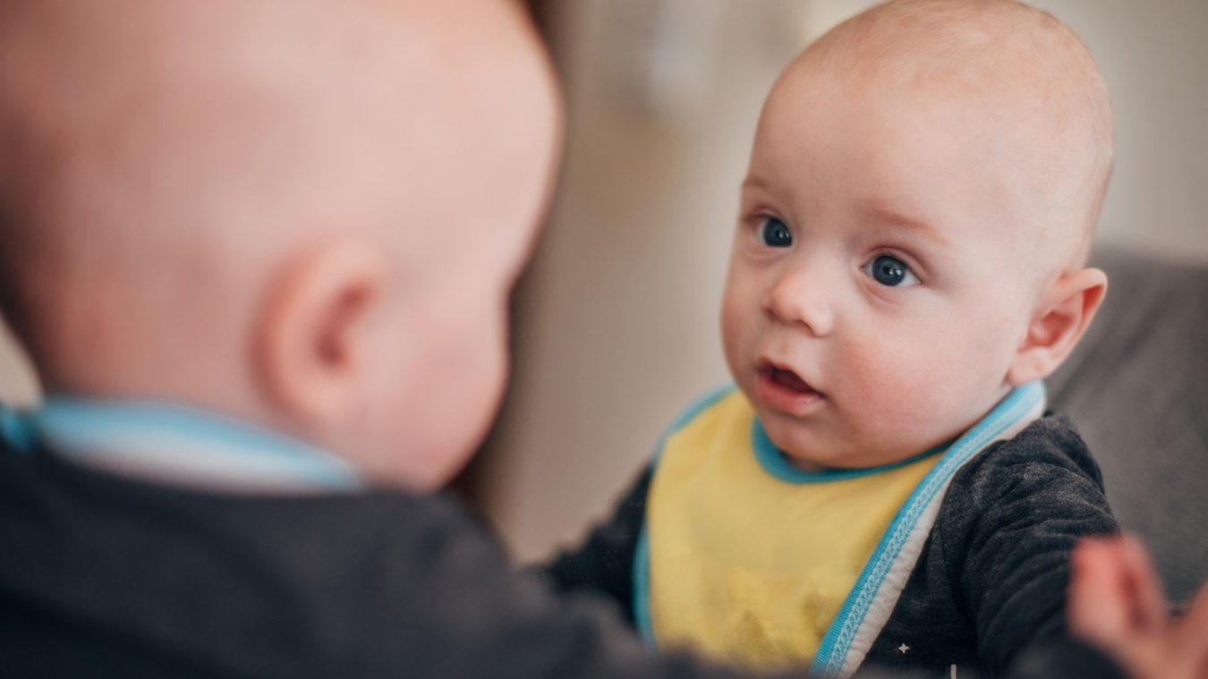 Baby looking at their reflection in the mirror.