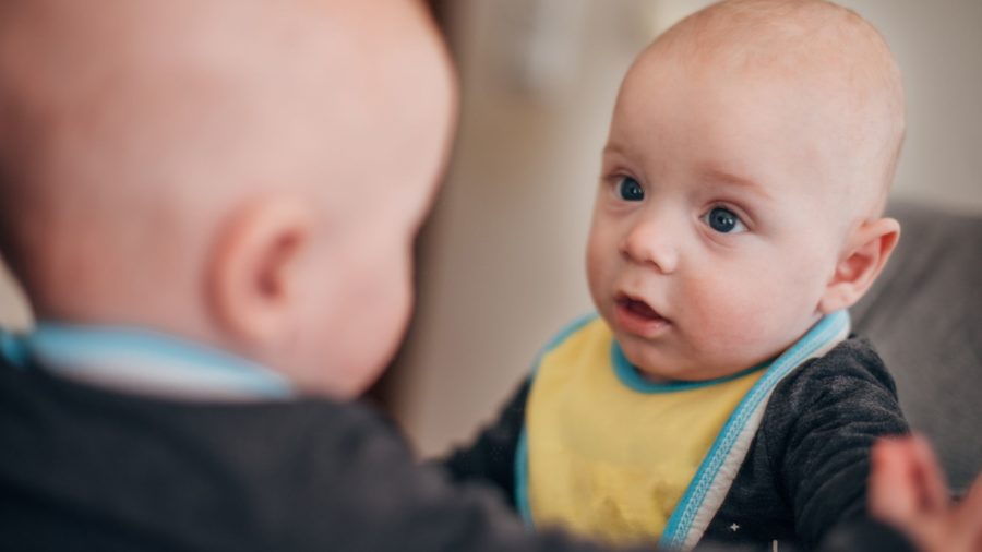 baby looking at a reflection of themself in mi