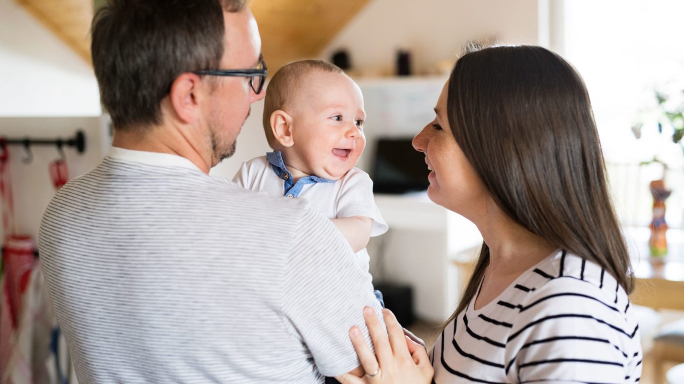 Baby in dads arms, smiling at Mum