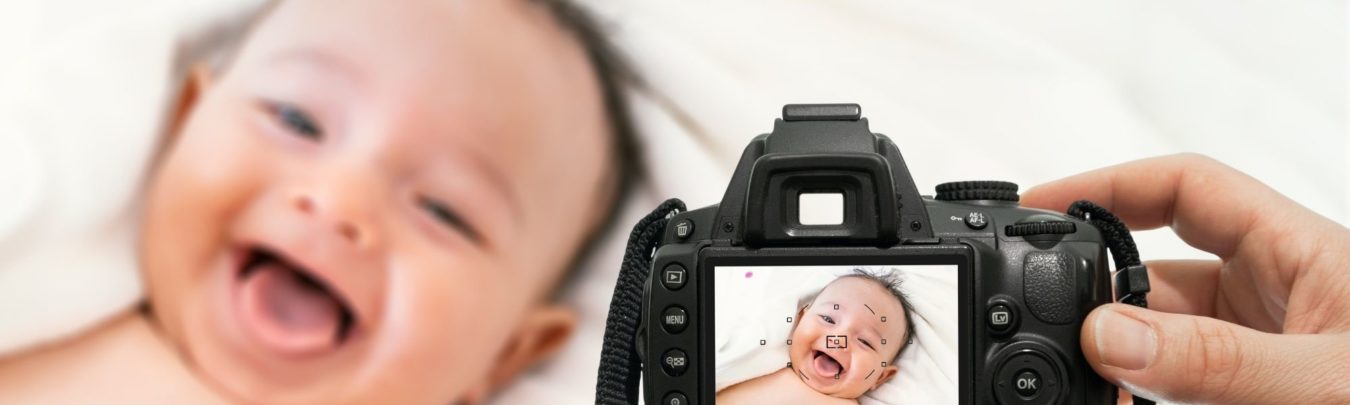 blog image showing the back of a DSLR camera screen, with a smiling baby in the background that has been captured by the camera