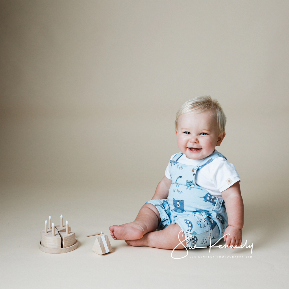 baby boy wearing dungaree's with a wooden birthday cake as a cake smash alternative photoshoot for his first birthday