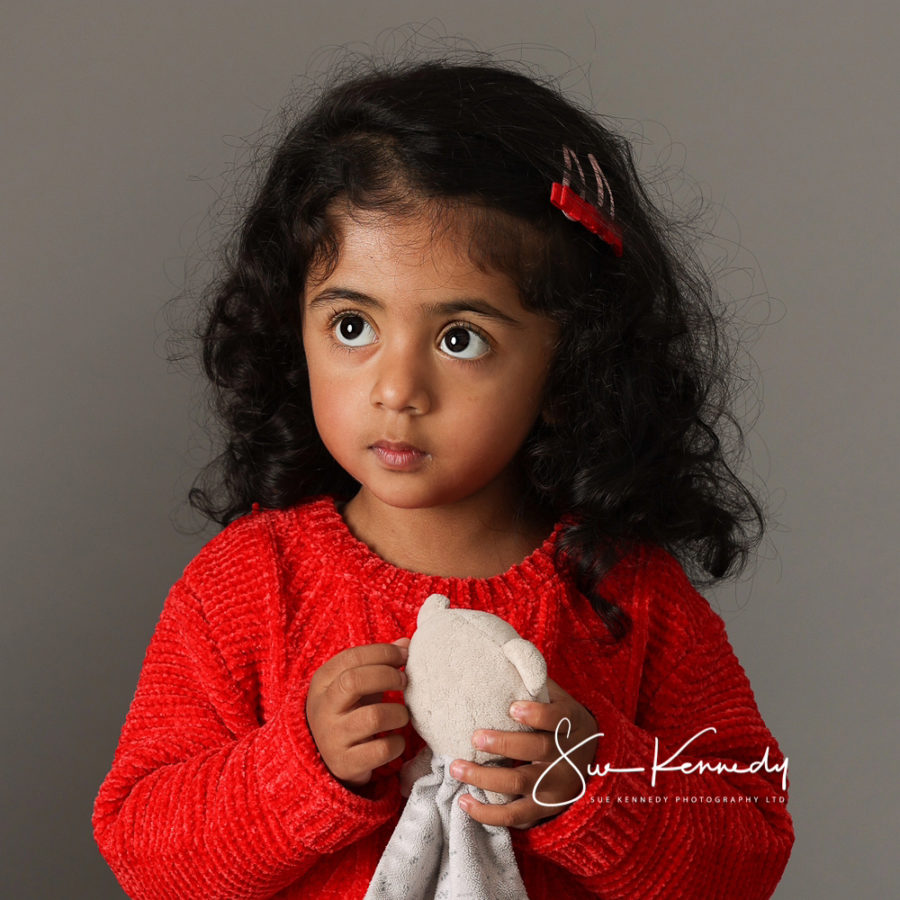 Toddler girl holding her soft bear comforter in both hands and looking off to the side.