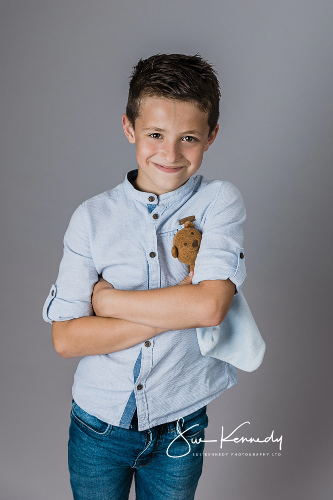 smiling young boy with folded arms photographed with his favourite toy tucked under his arm