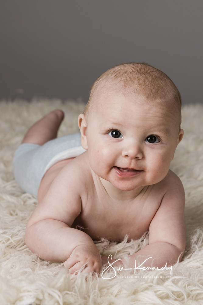 5 month old baby boy lying on his tummy on a wool rug lifting his head and smiling