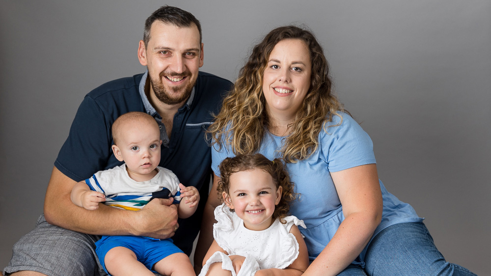 Family of two parents and two children sat looking toward camera