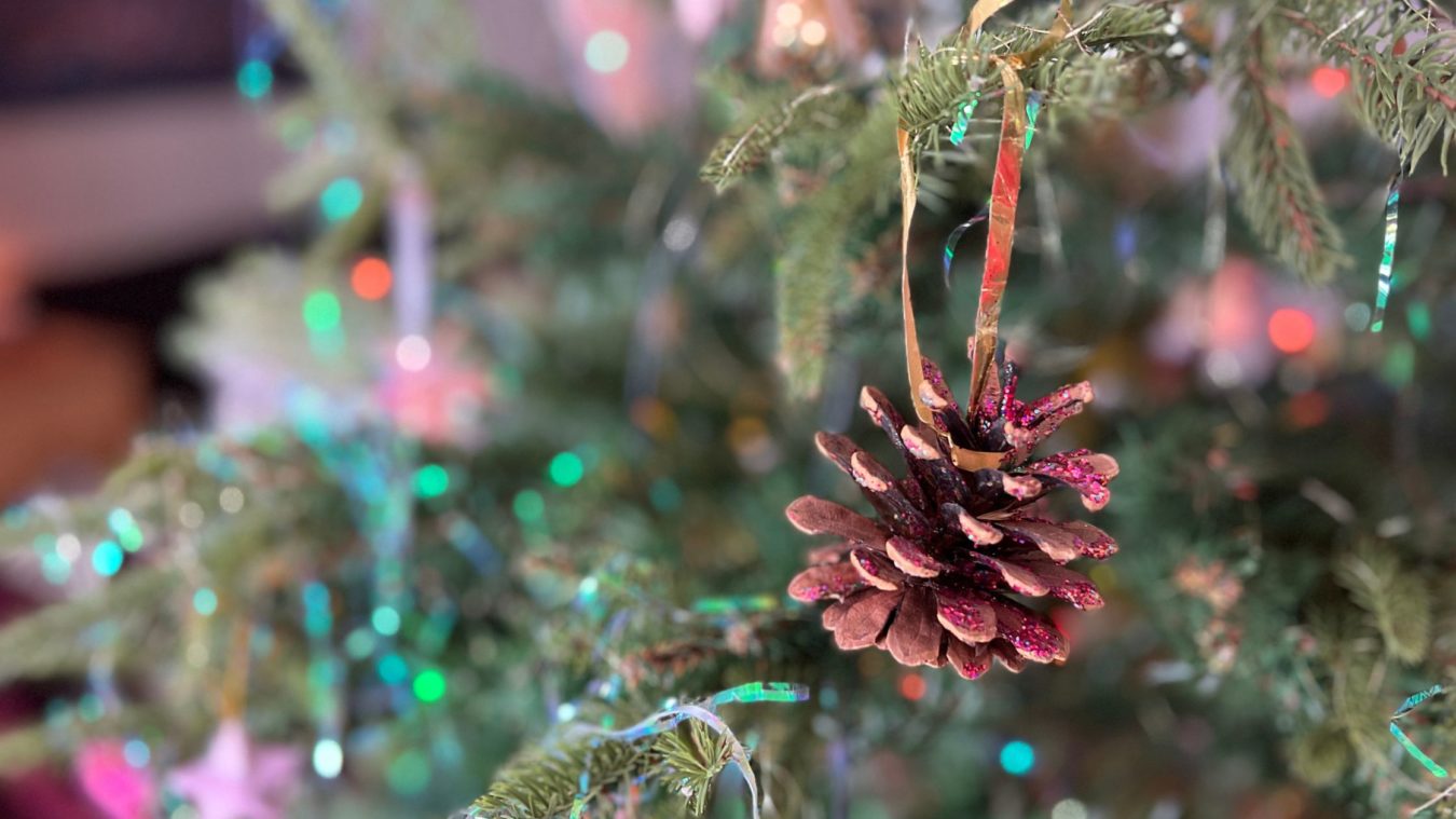 A child's pinecone decorated with glitter hanging on the family Christmas tree at home.