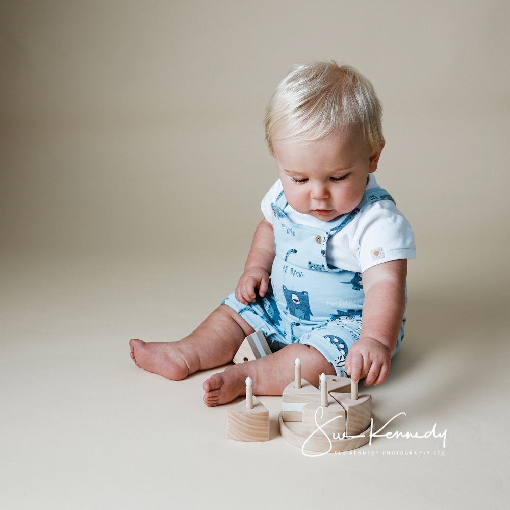 First birthday baby portrait in a neutral studio setting, featuring a one-year-old baby sitting with simple wooden birthday cake.