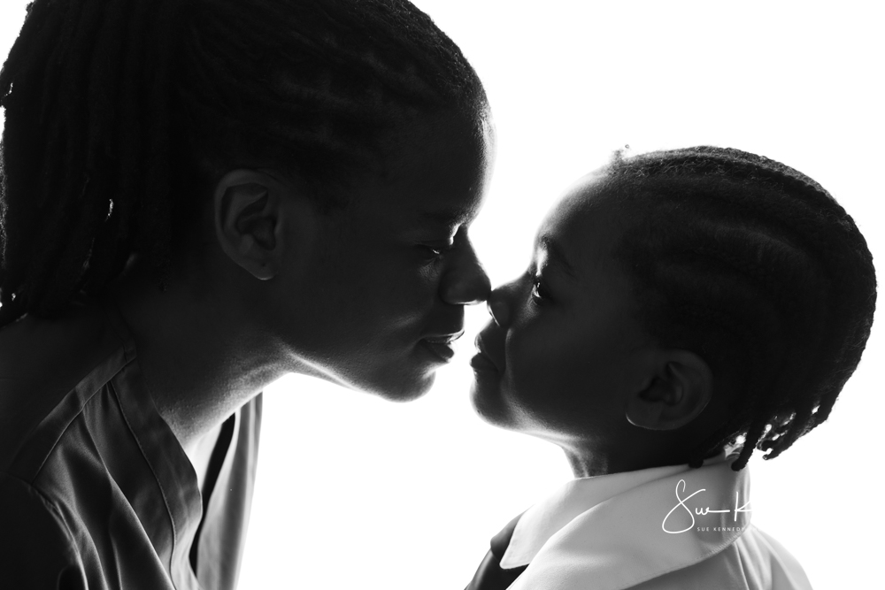 Silhouette-style studio portrait of a parent and child touching noses and looking at each other.