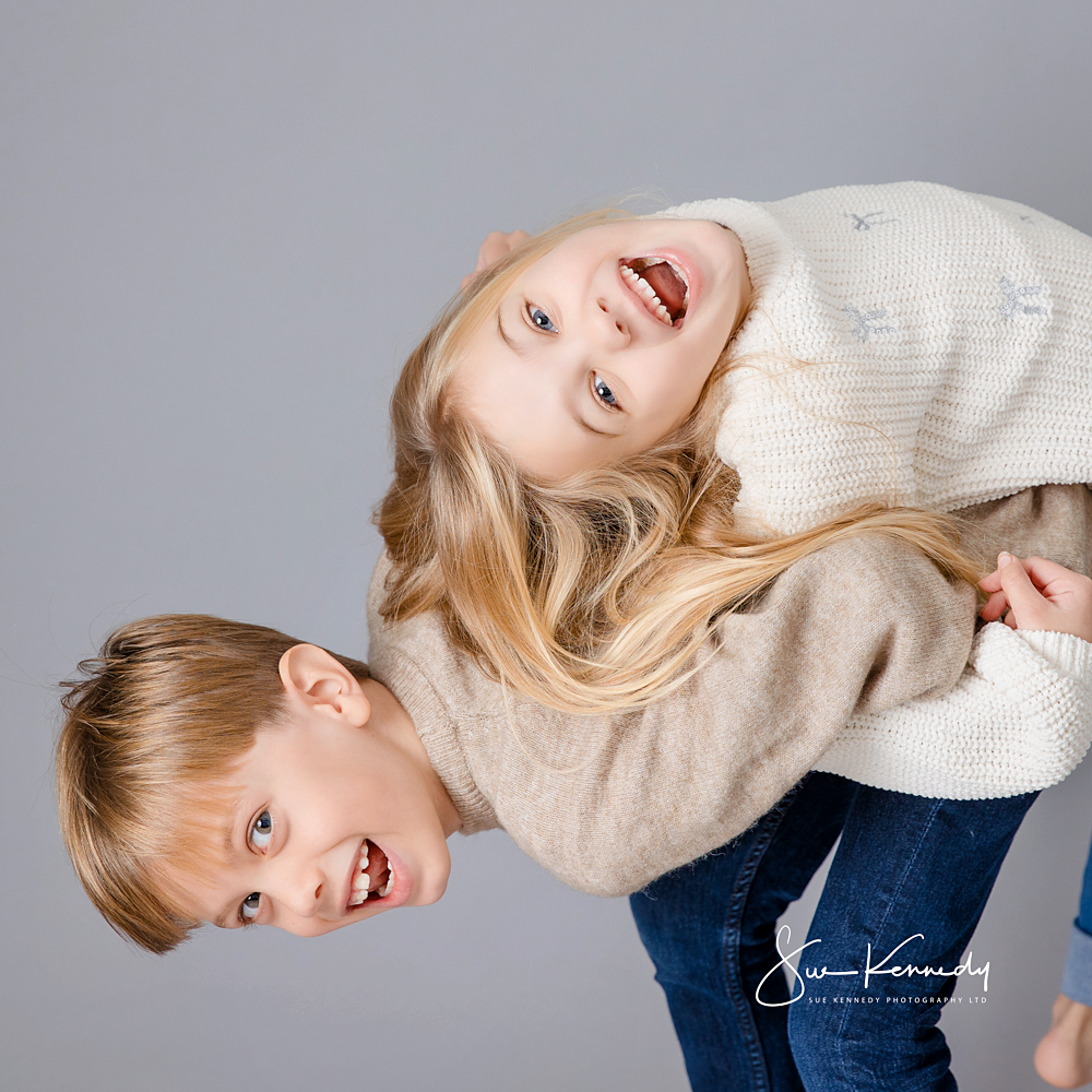 Brother and sister laughing together during a relaxed, child-led portrait session at Sue Kennedy’s Harlow studio, showing their natural connection and playful personalities.