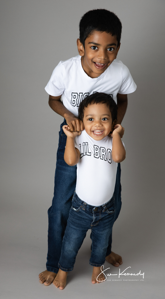 wo brothers smiling during a relaxed, child-led portrait session at Sue Kennedy’s Harlow studio, wearing matching ‘Big Bro’ and ‘Lil Bro’ outfits and showing their close bond.
