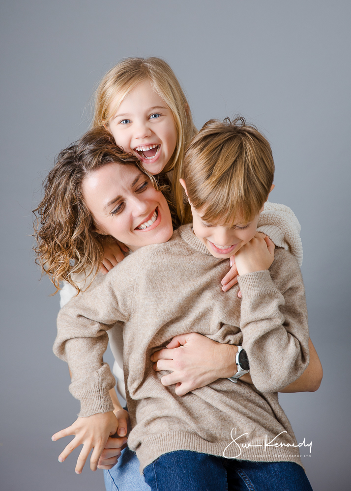 Mother laughing with her two children during a relaxed studio portrait session in Essex, showing their natural connection and playful personalities.