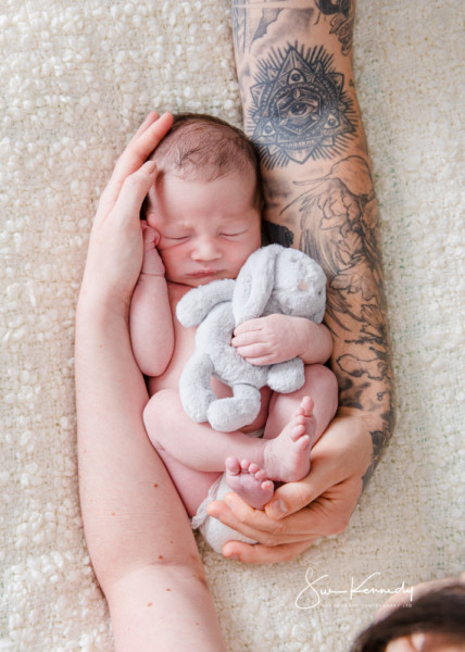 Young baby asleep in their parents’ arms, photographed naturally in a relaxed studio setting in Harlow.